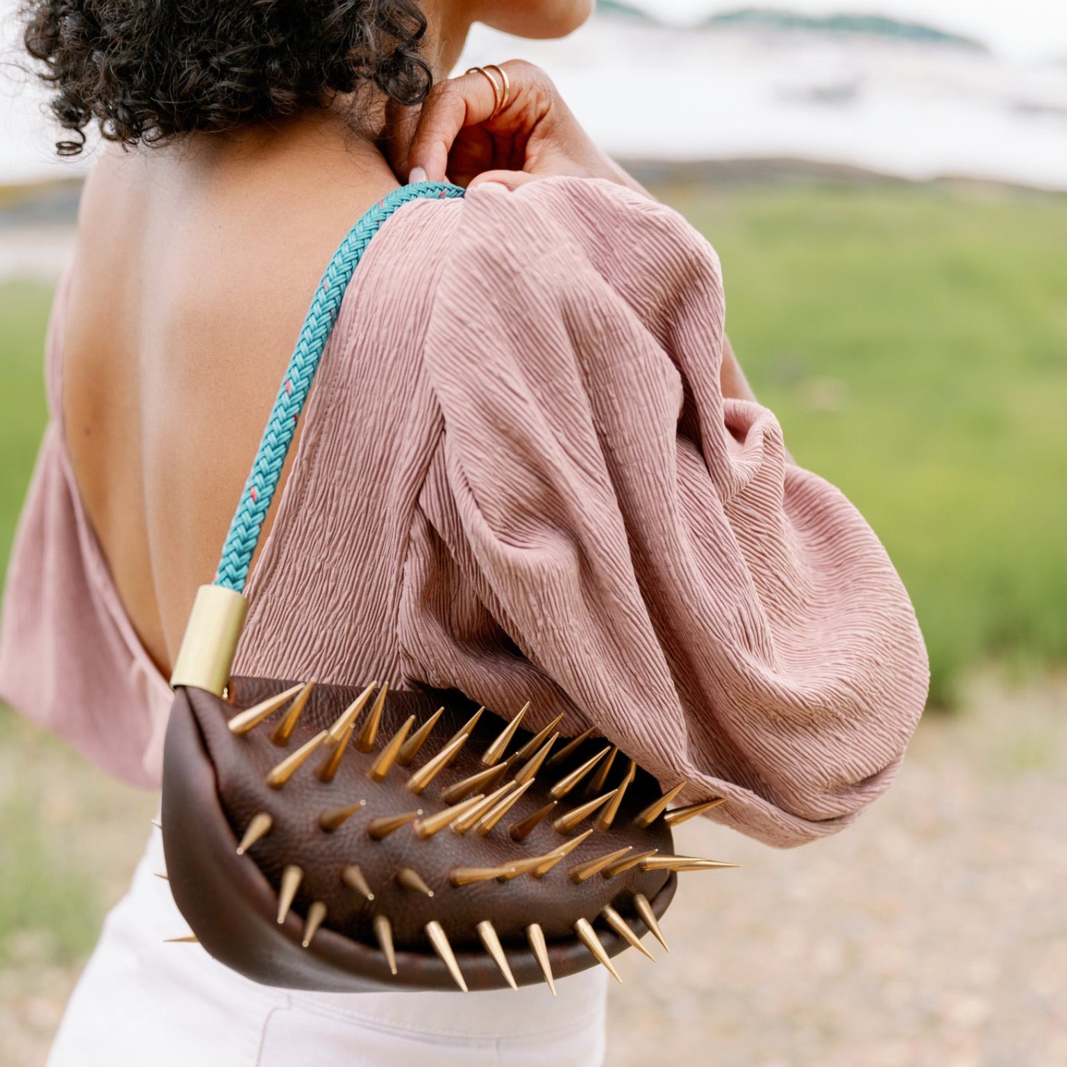 Person wearing a brown leather handbag with brass spikes at the beach