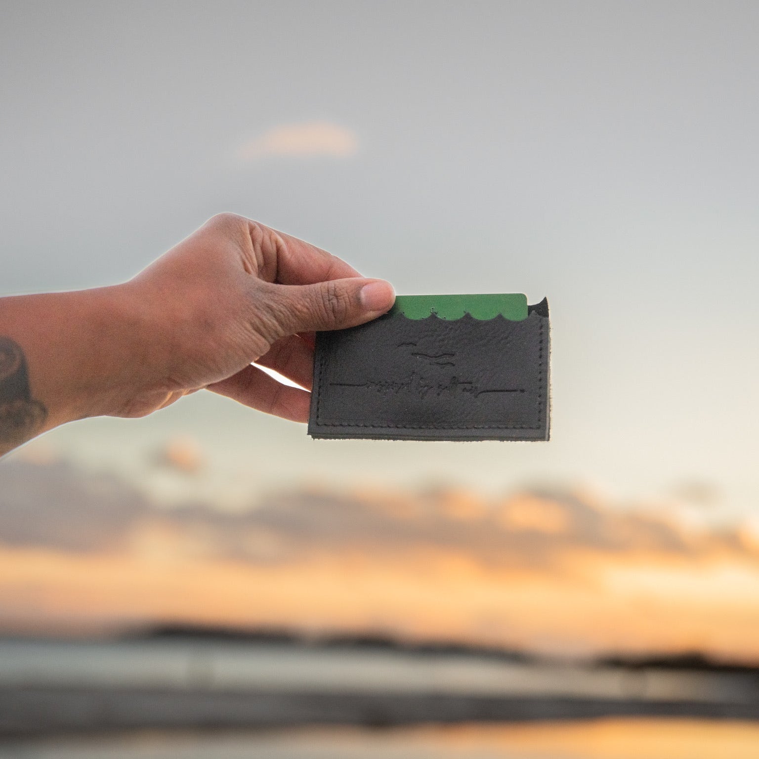 Hand holding a black wallet with a sunset in the background