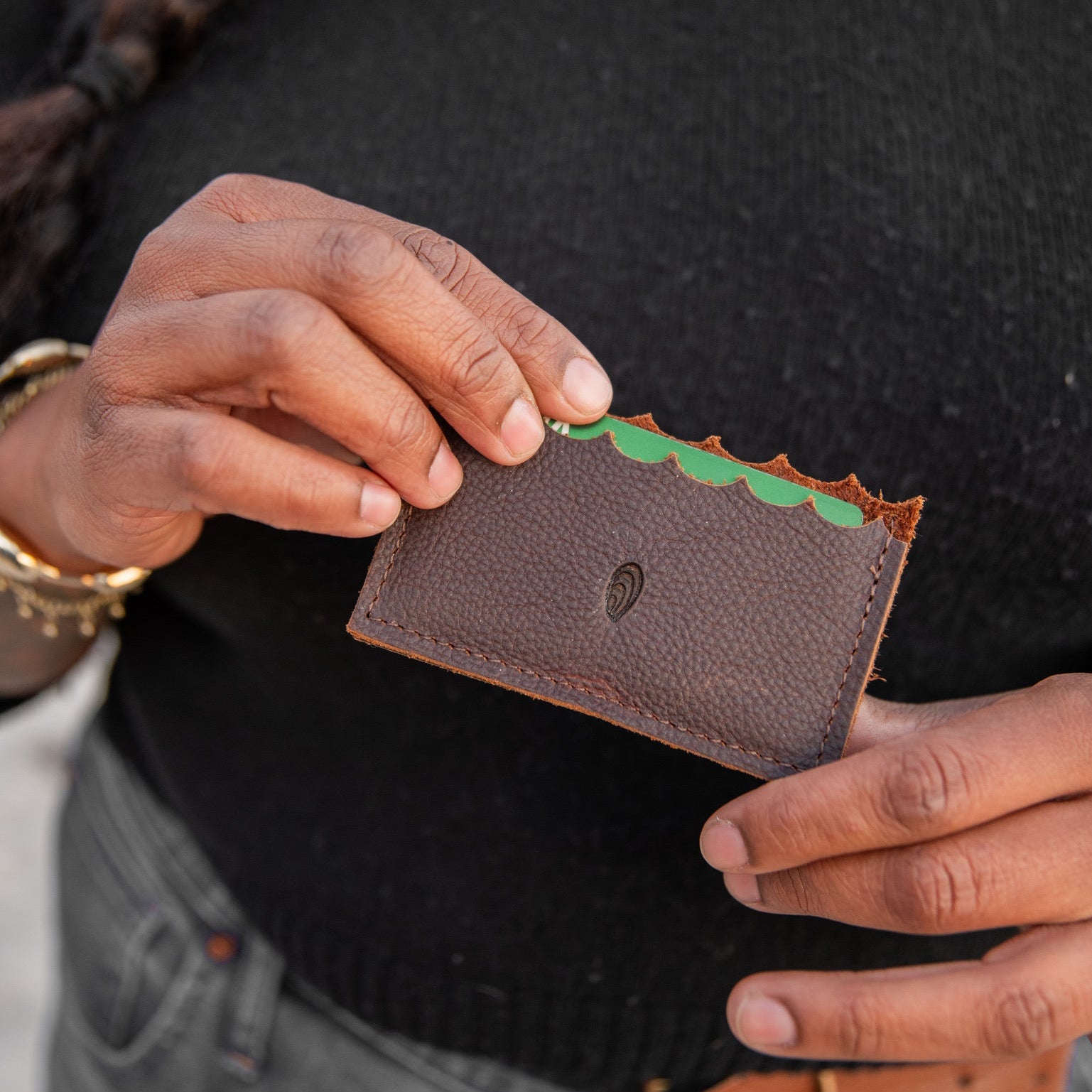 Person holding a brown leather cardholder with a green interior.
