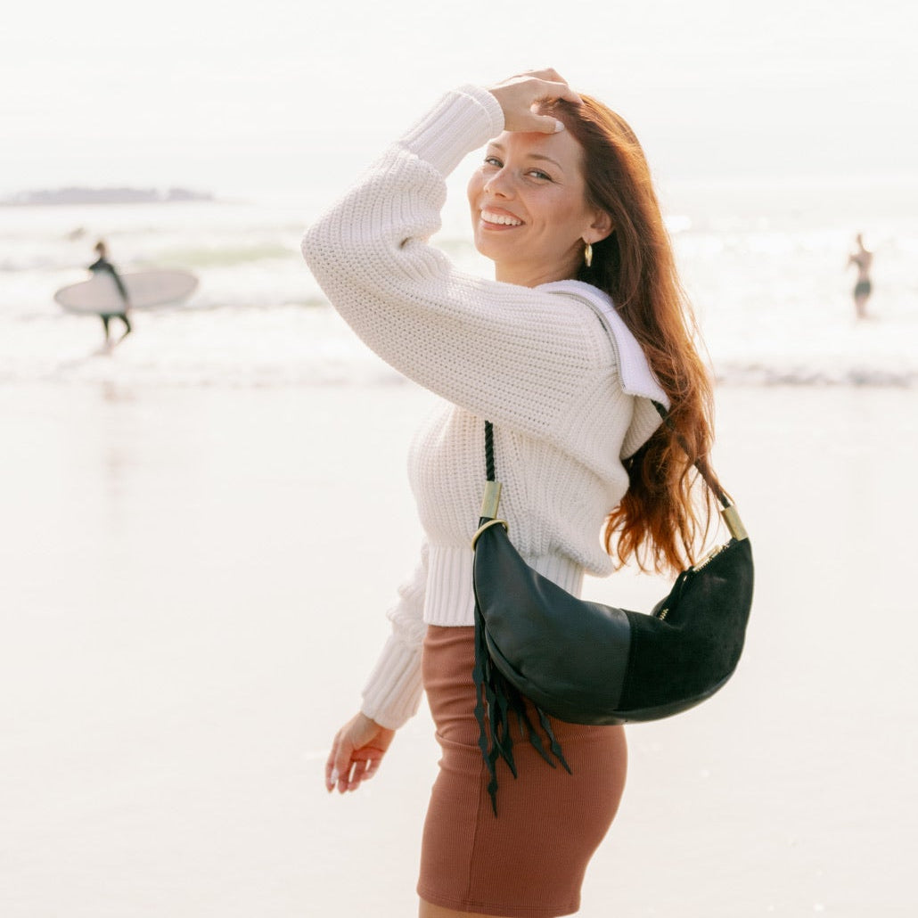 Woman walking on a beach with a black leather sling bag with a blurred background