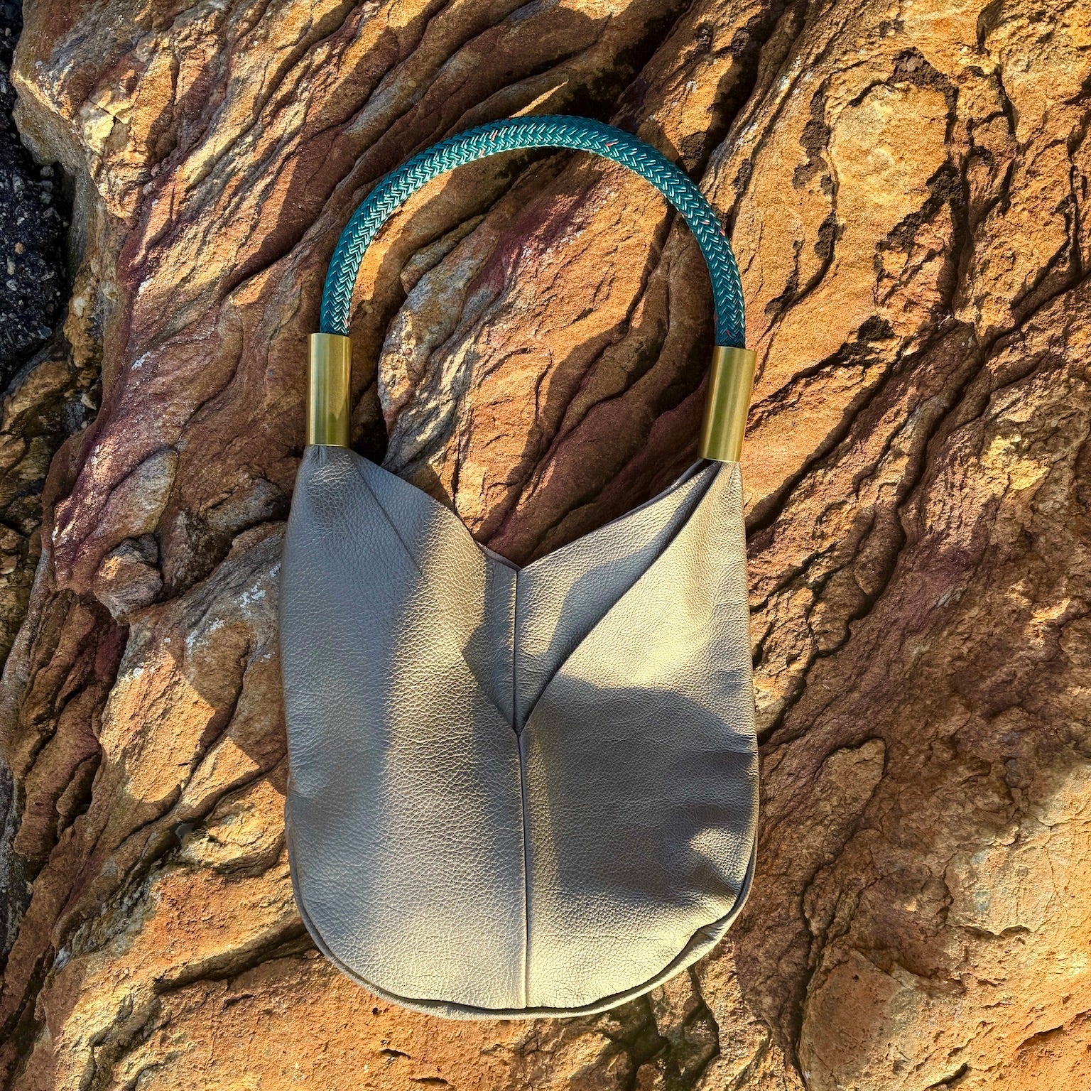 Metallic handbag with teal cord and gold clasp on a textured rock surface