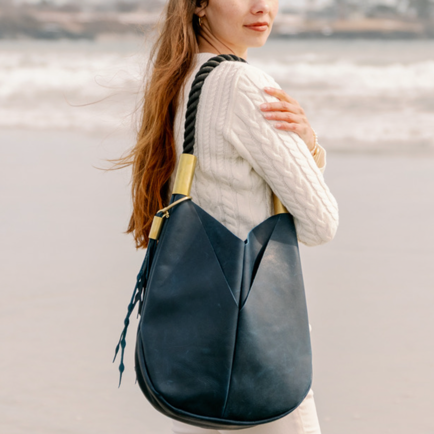 Woman standing on a beach with a navy bag over her shoulder