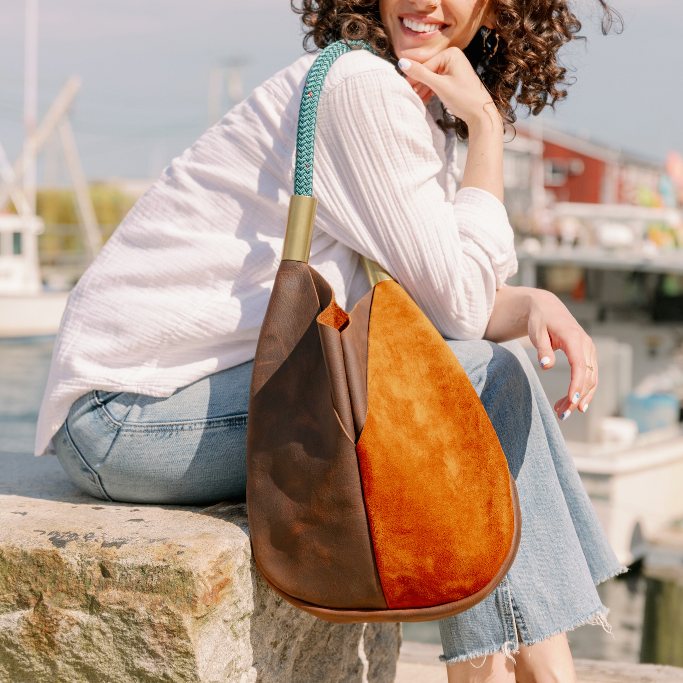 Woman sitting by a waterfront with a brown and orange leather handbag