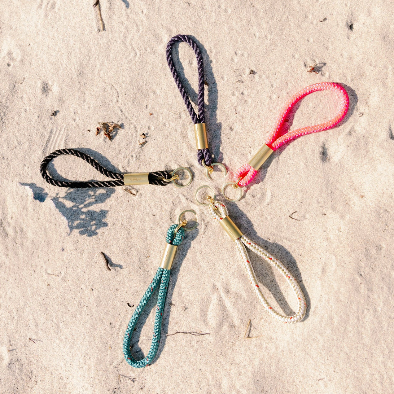 Five rope keychains of different colors on a sandy surface