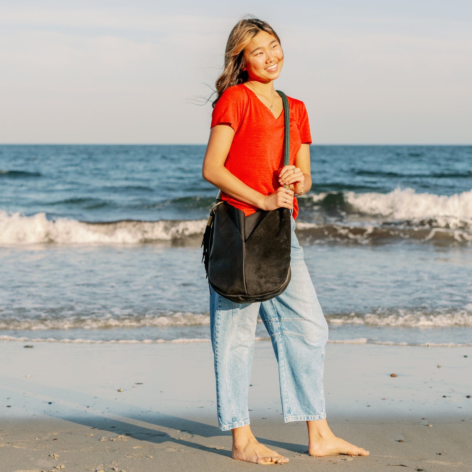 Person holding a black bag on a beach with ocean waves in the background