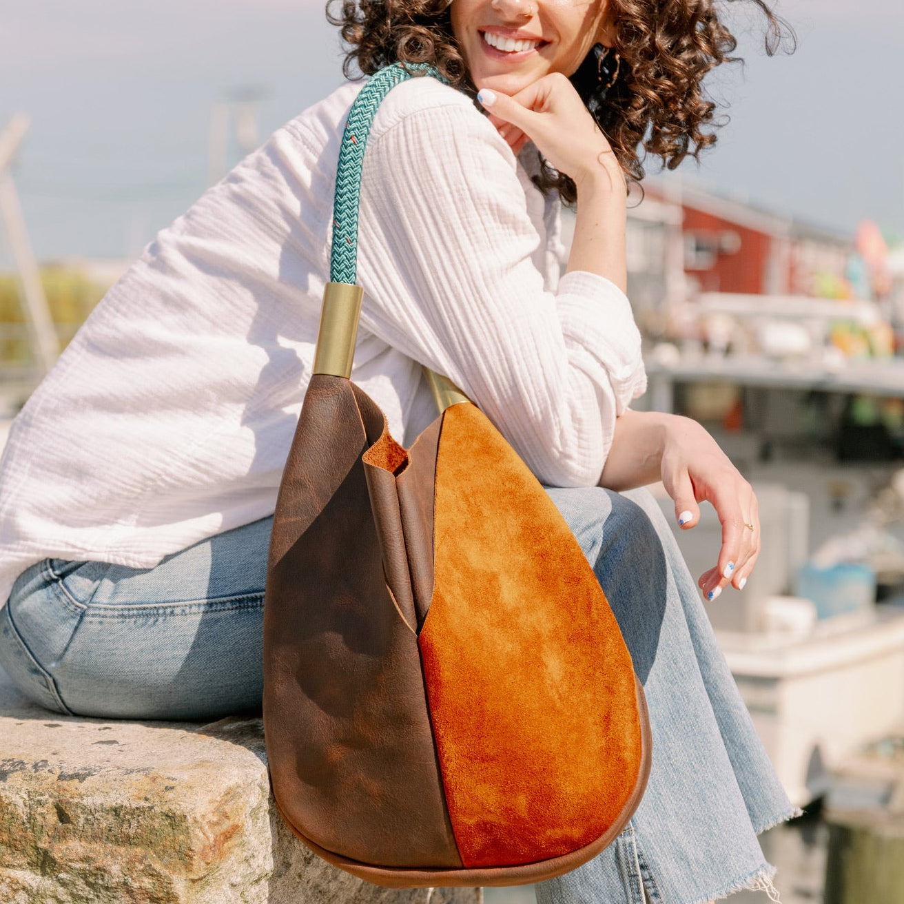 Woman holding a two-toned brown and leather bag by a waterfront with boats in the background