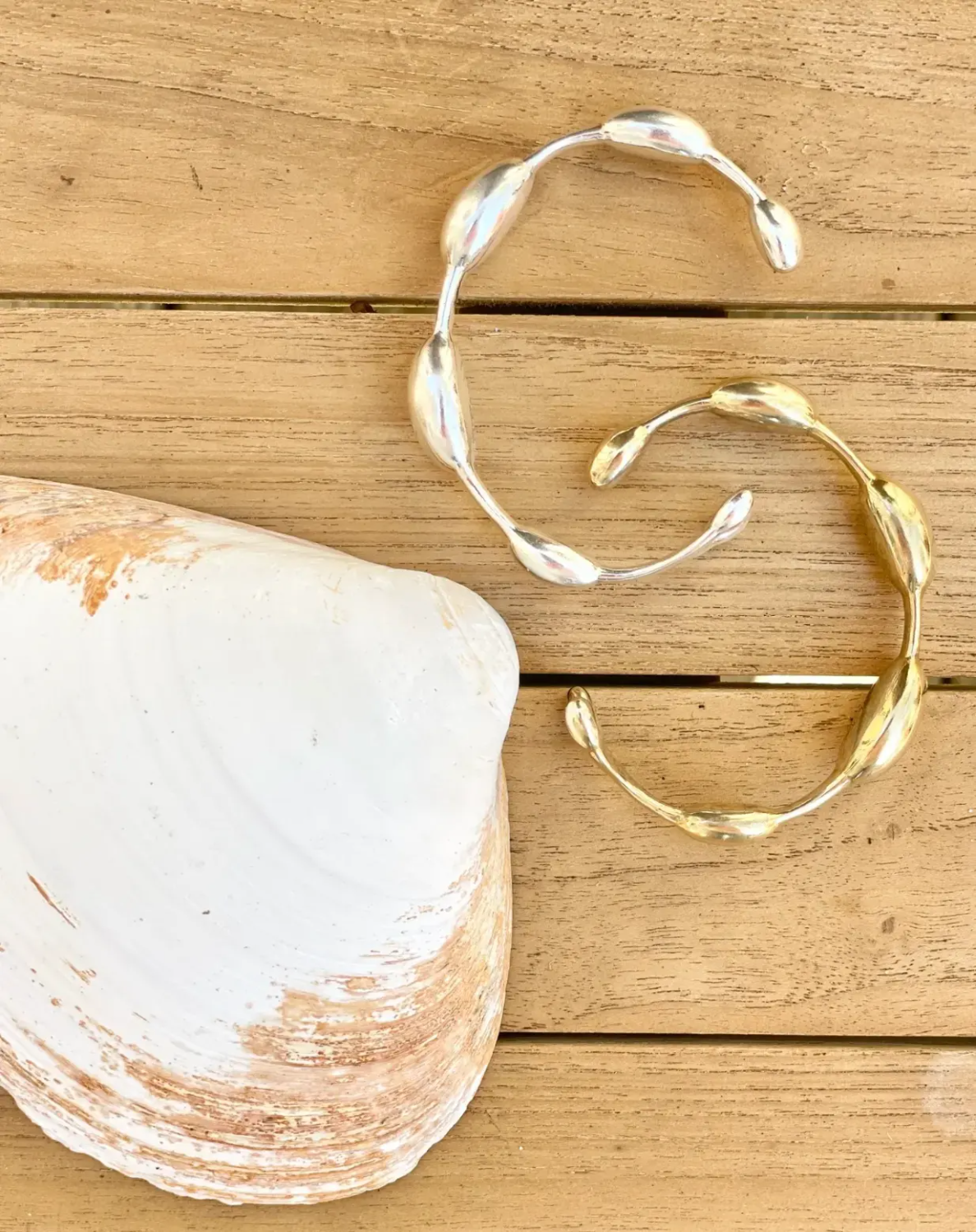 gold and silver seaweed bracelets by a clam shell