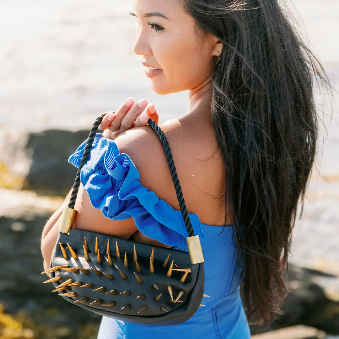 Woman holding a black handbag with gold spikes by the ocean