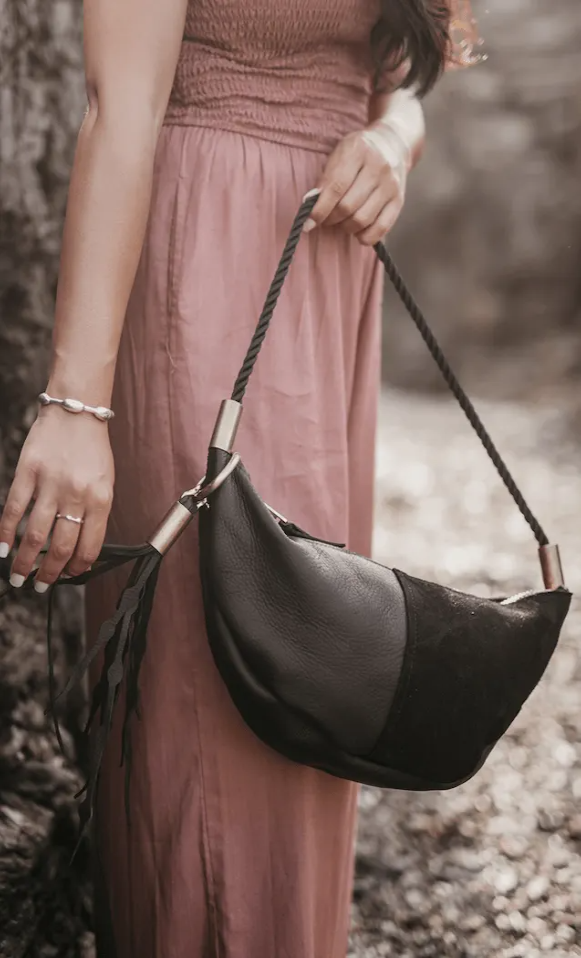 Person holding a black handbag with a blurred natural background