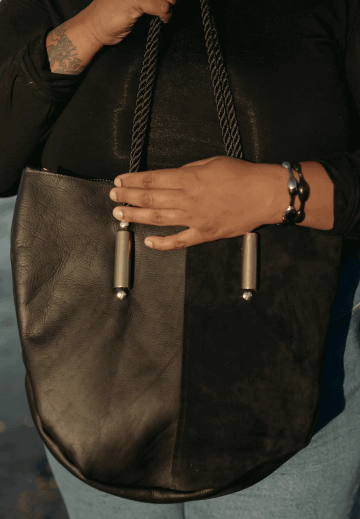 Person holding a dark black leather handbag with a textured surface.