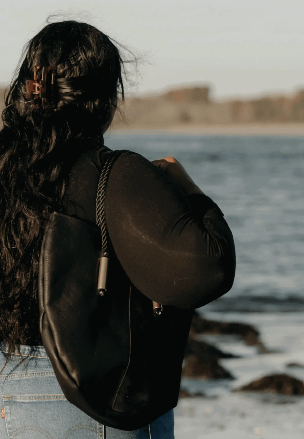 Person with a black backpack standing by the water