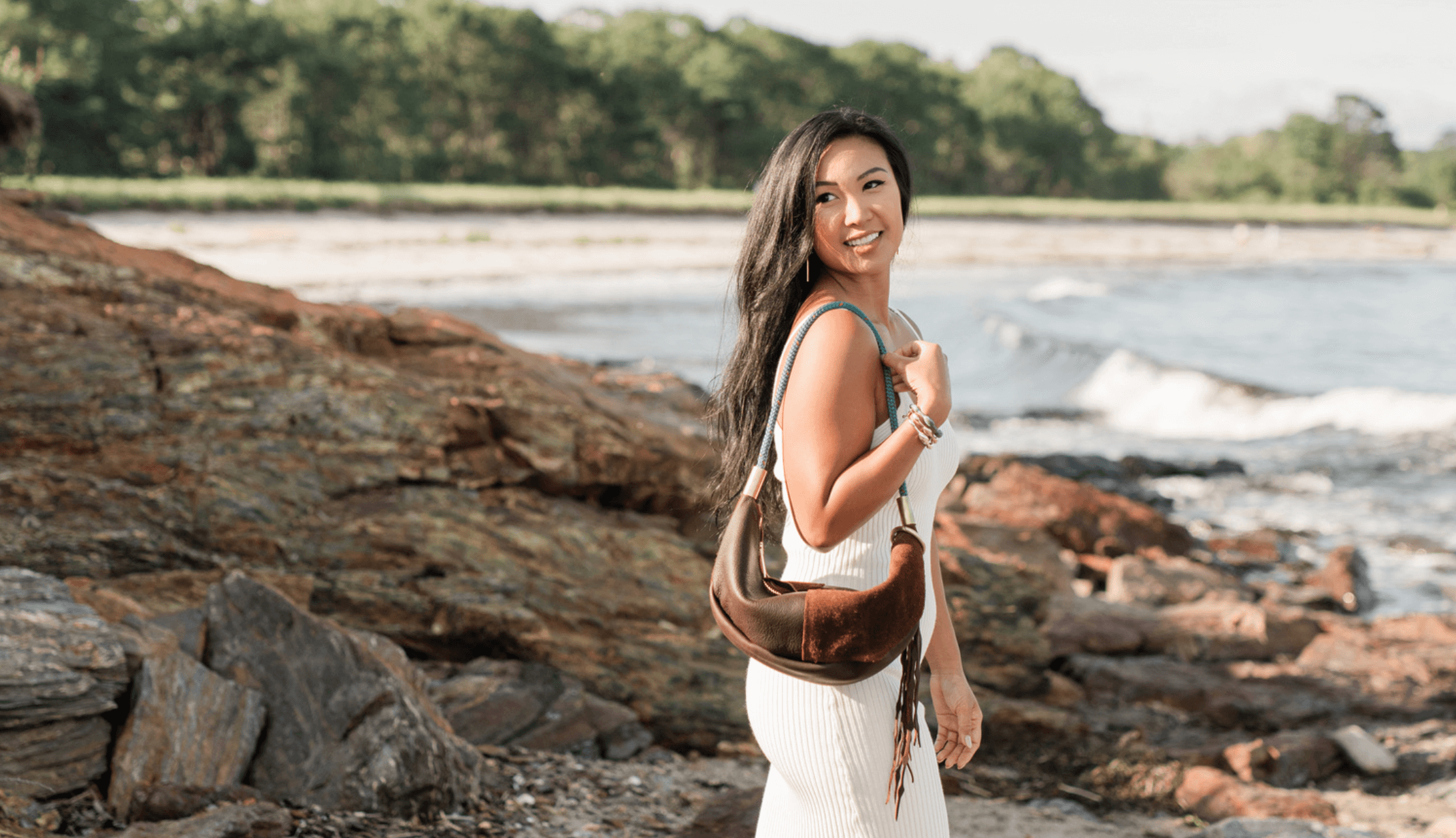woman wearing a brown leather sling bag on the rocky coast