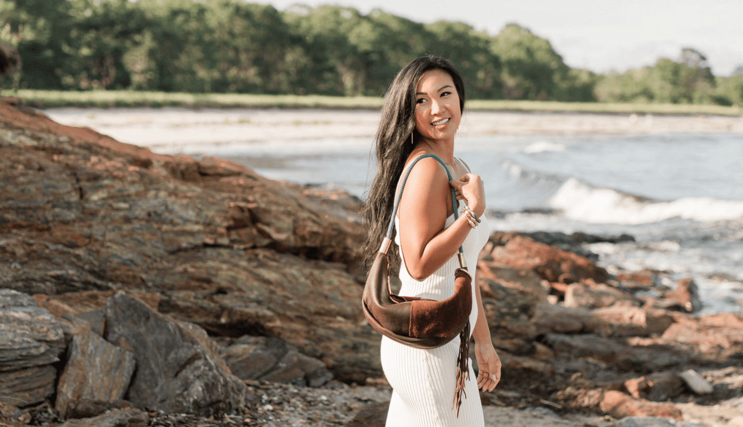 woman wearing a brown leather sling bag on the rocky coast