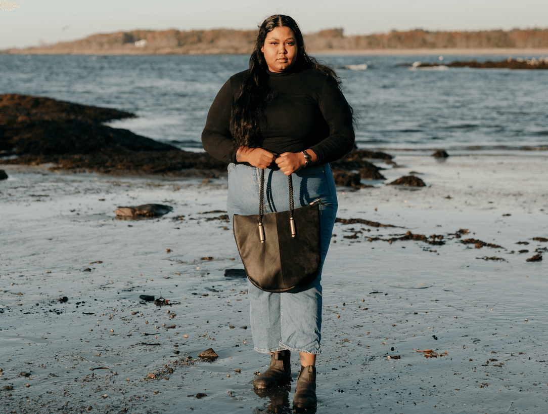Woman on the beach carrying a black zip leather tote