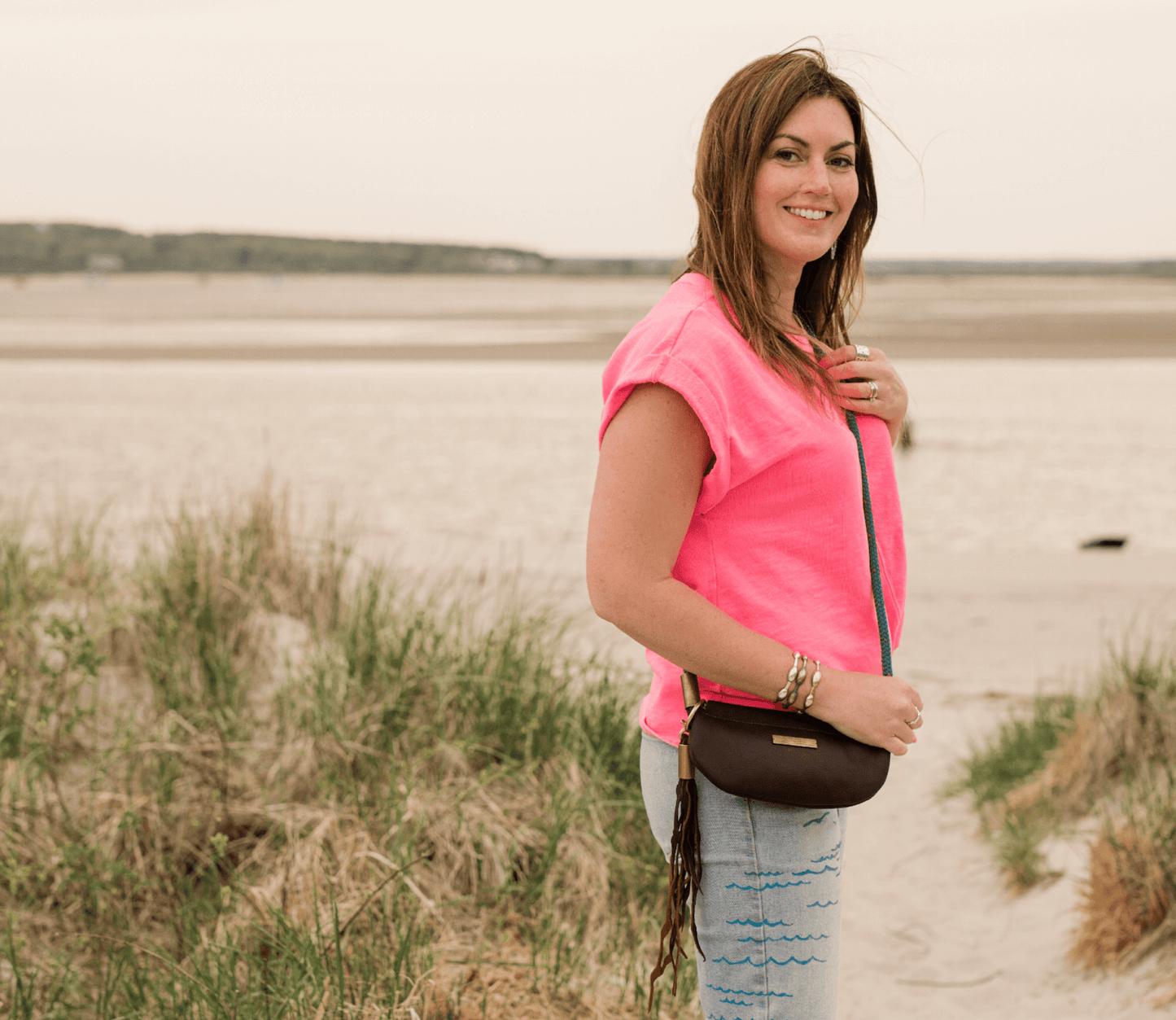 woman on the beach in the harbor wearing a gold crossbody leather bag