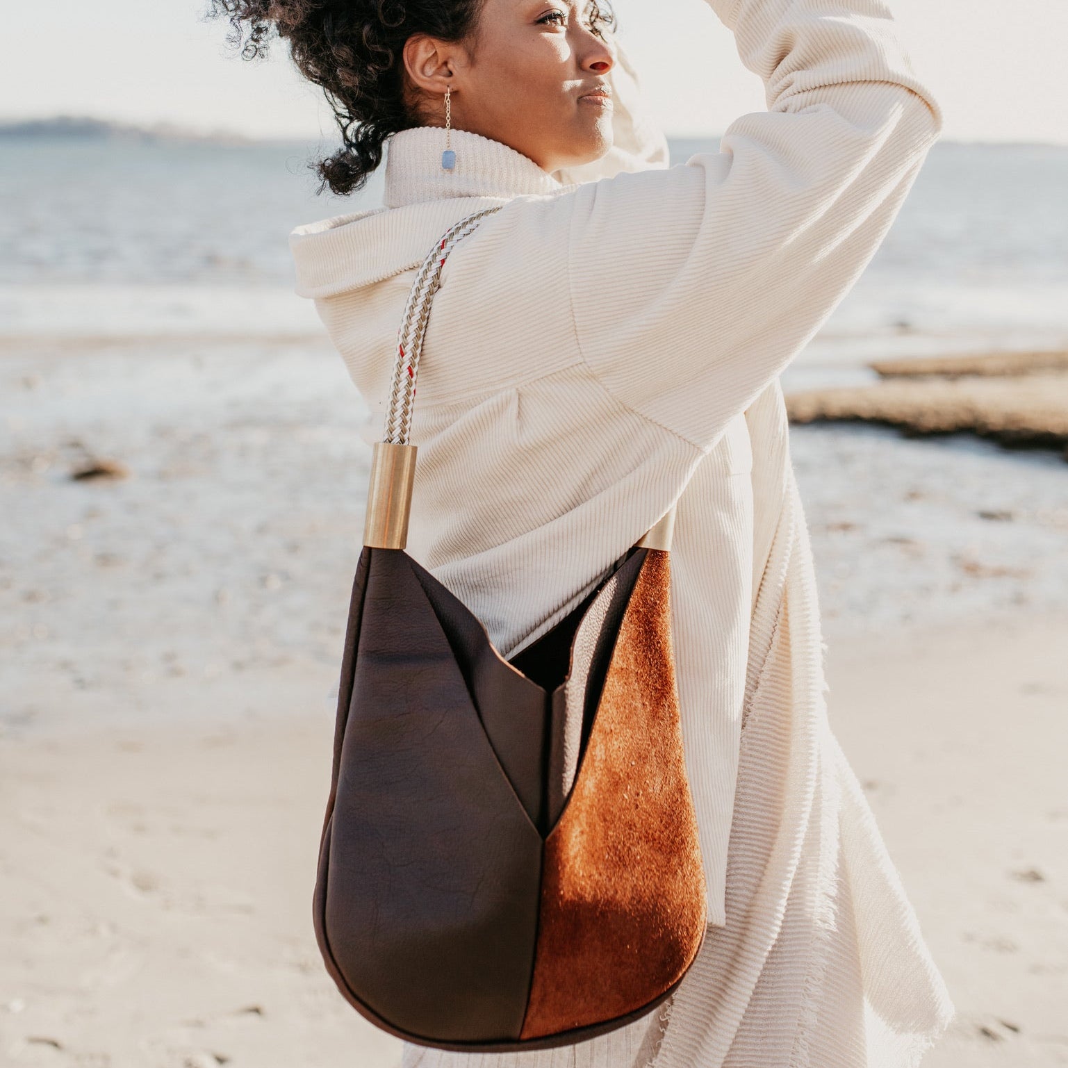 Woman on a beach wearing a white outfit with a brown leather and suede handbag.