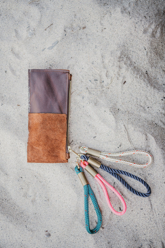 brown leather clutch on the sand with variously colored rope wristlets