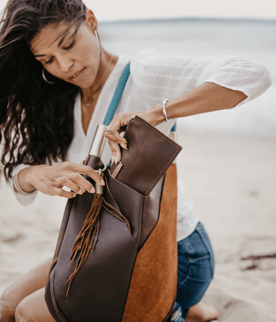woman inserting a leather clutch into her leather bag on the beach
