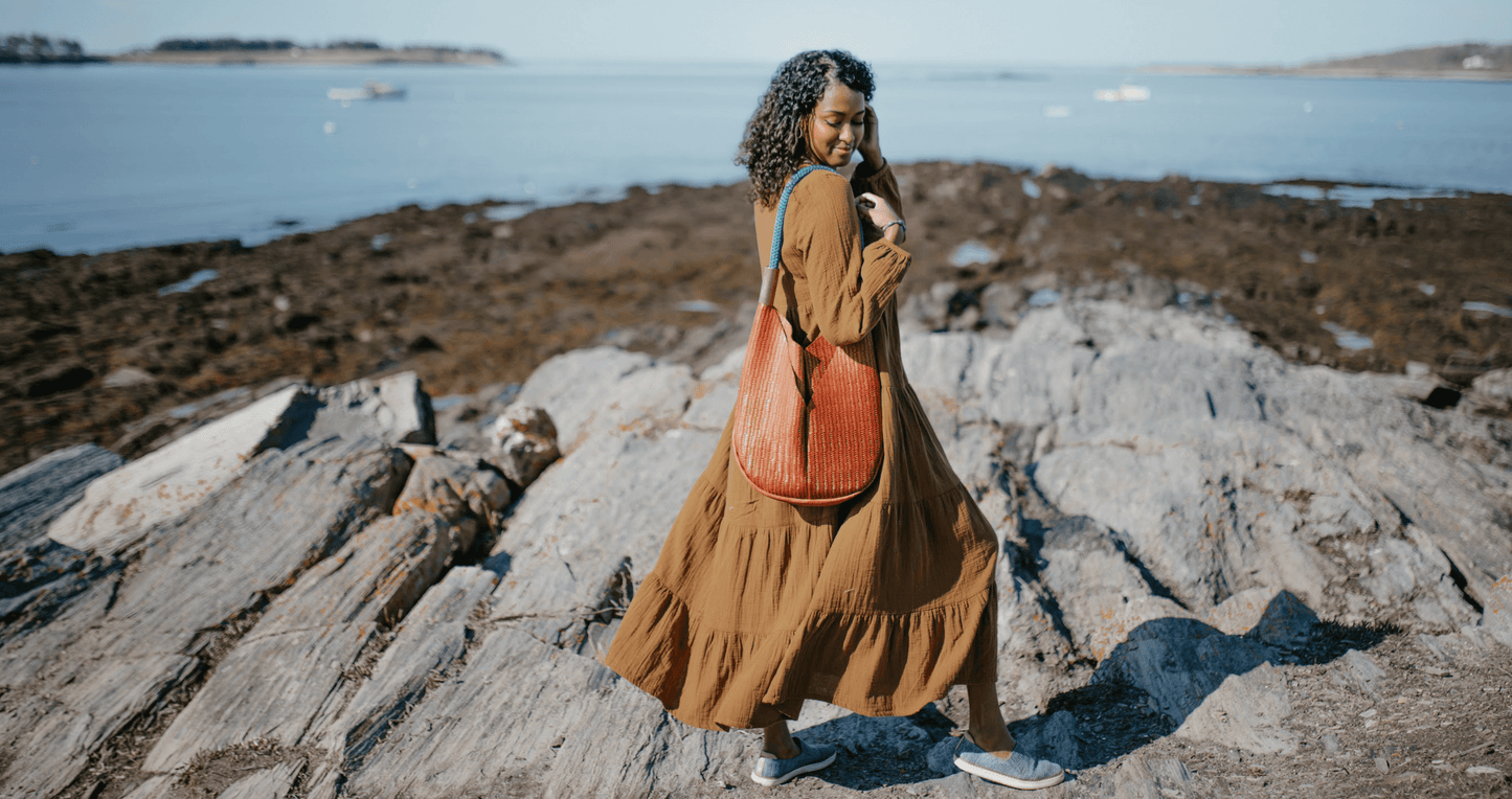 Woman walking on rocky beach wearing brown basketweave leather tote