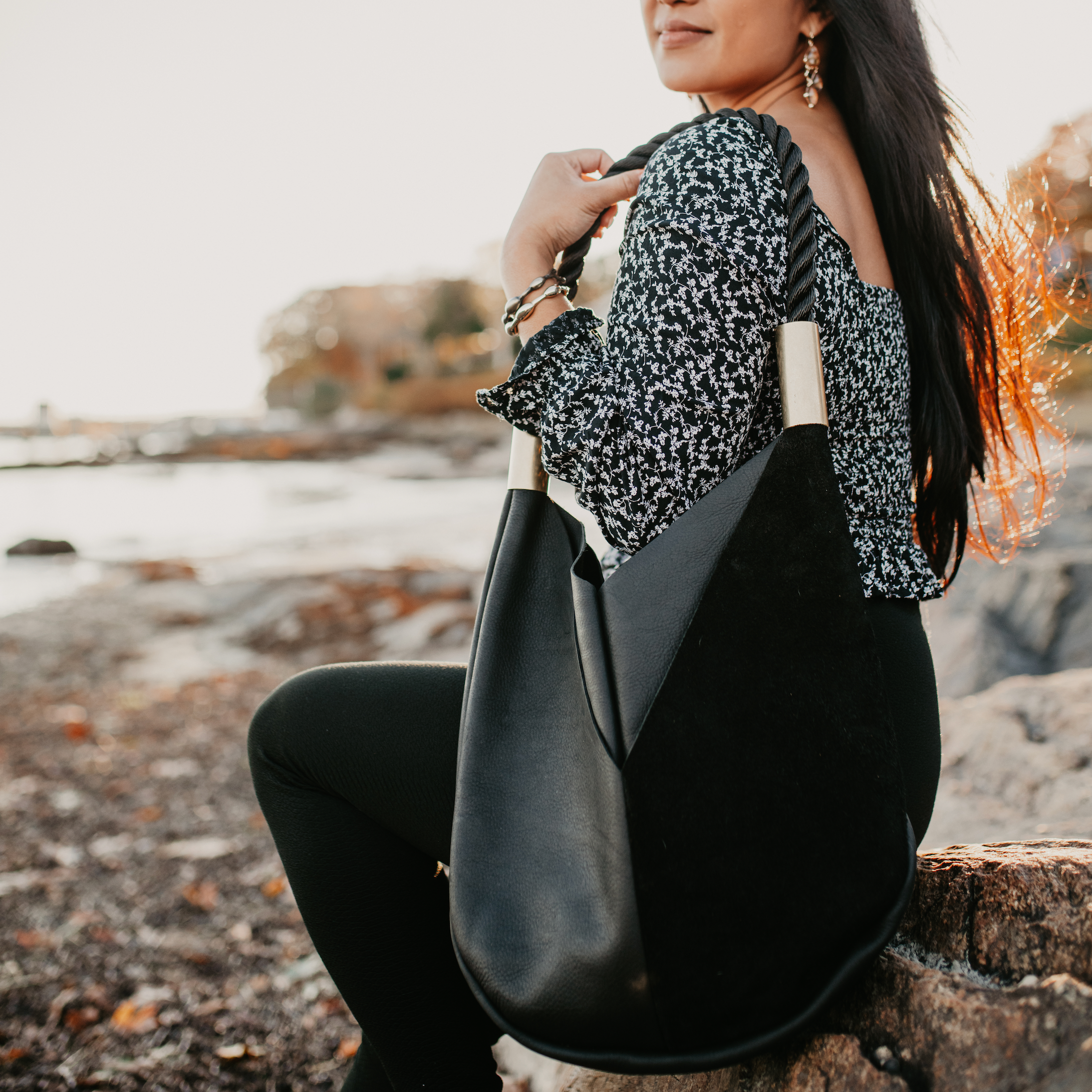 Woman holding a black leather handbag by the seashore
