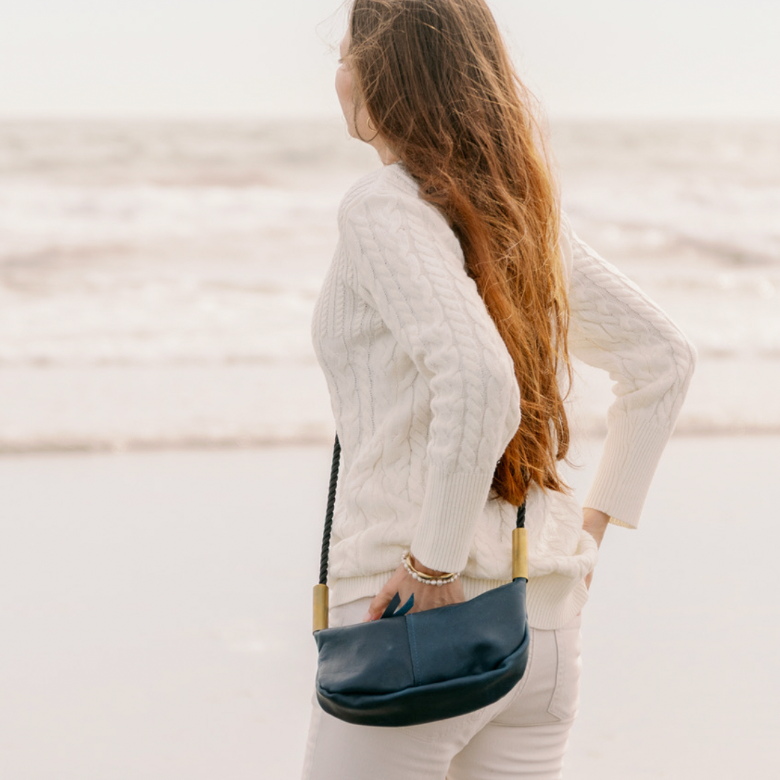 Woman standing on a beach holding a navy bag