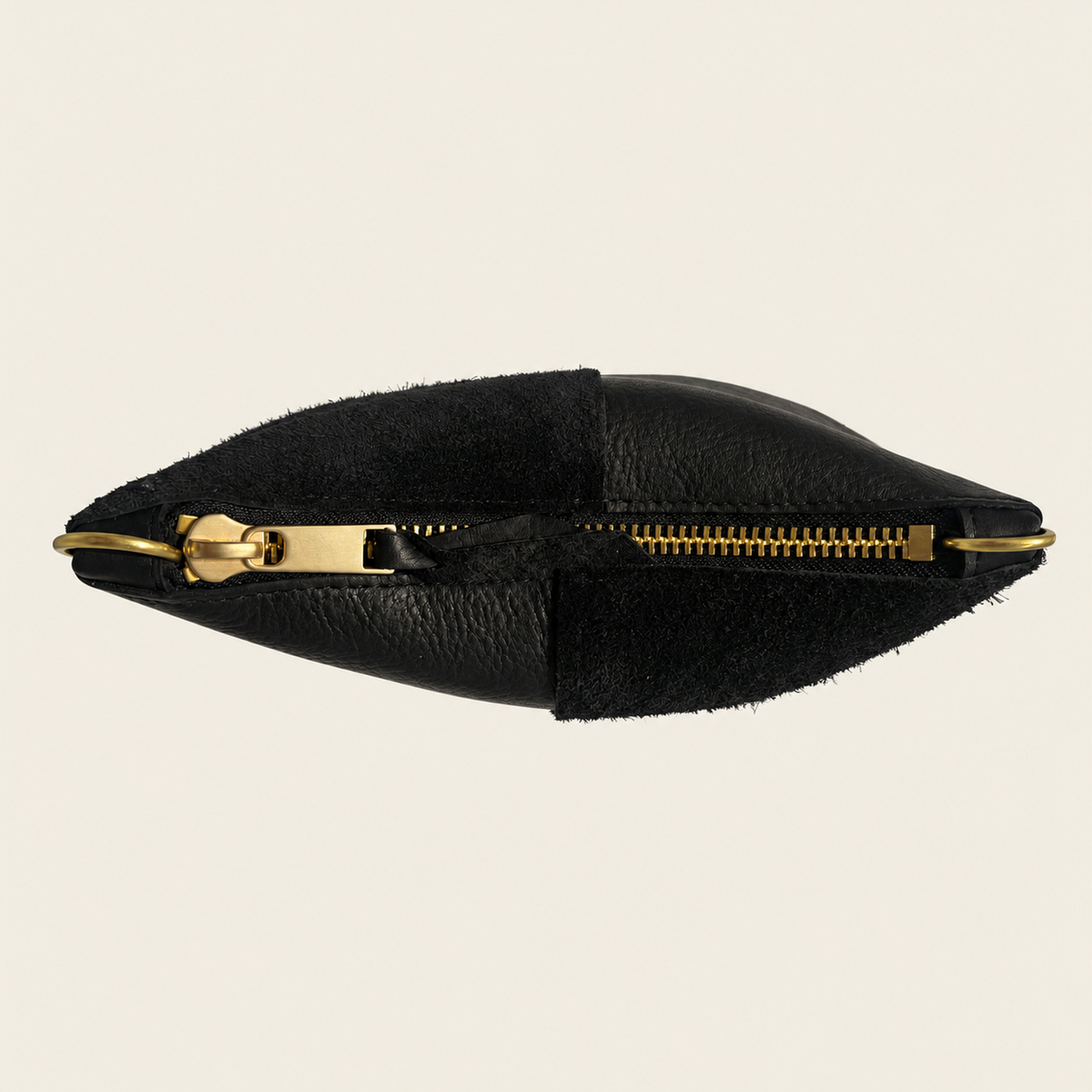A black leather and suede pouch with a gold-tone zipper and pull, shown from a top-down view on a light beige background.