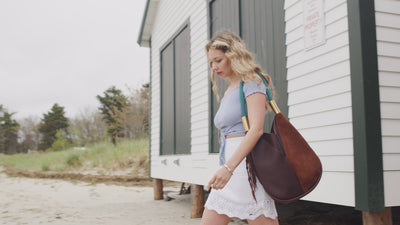 Woman wearing a brown leather tote walking along the beach