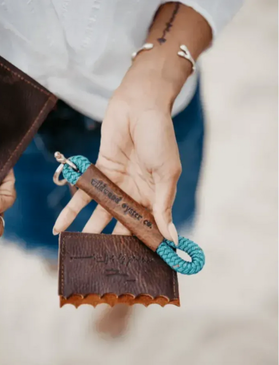 Person holding a leather wallet with a blue rope keychain, brand 'Vilkenkind' visible.